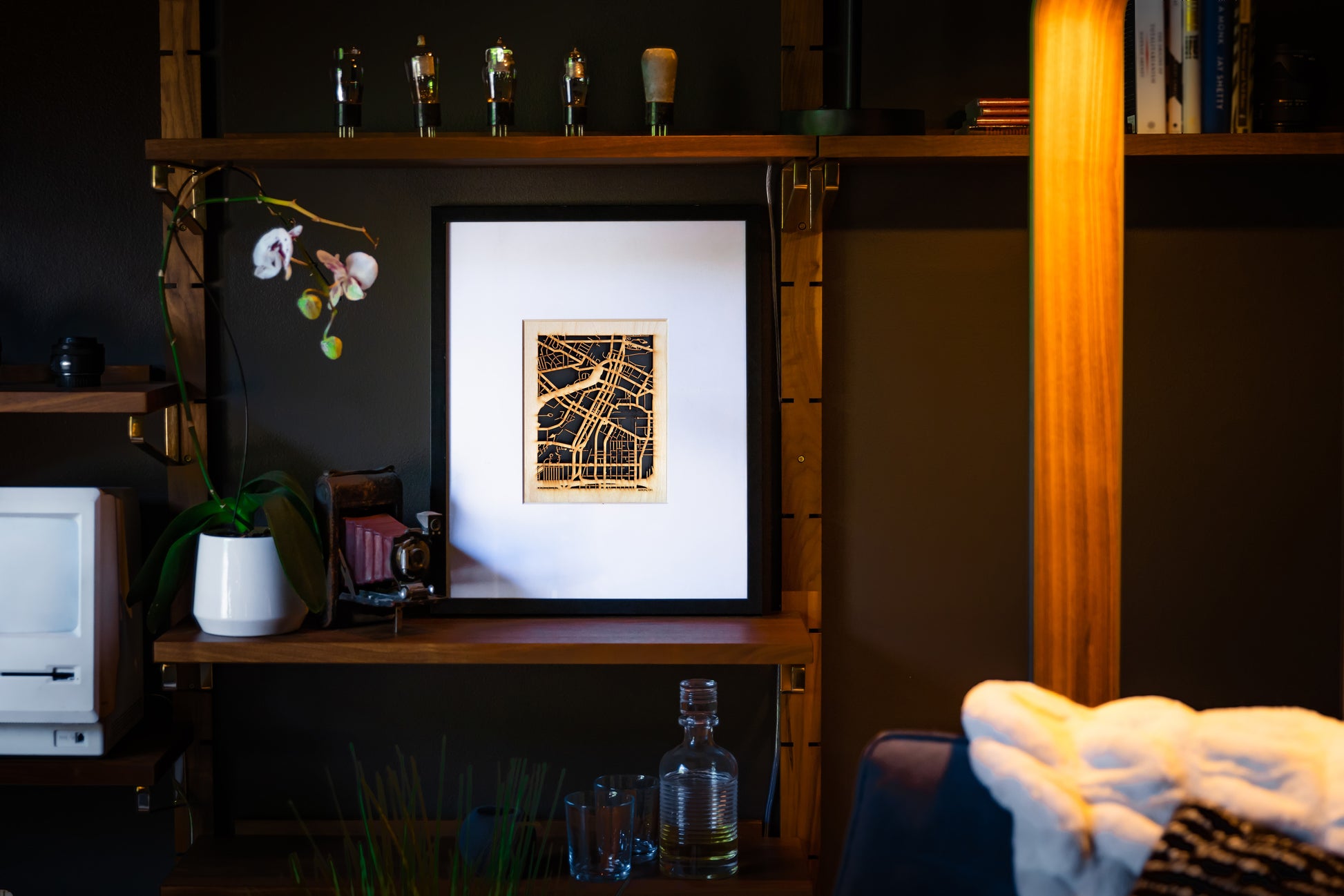Framed artwork on a shelf with decorative items in a dimly lit room