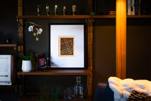 Load image into Gallery viewer, Framed artwork on a shelf with decorative items in a dimly lit room