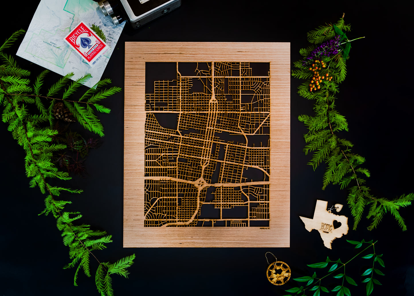 Wooden map art piece on a dark surface with greenery