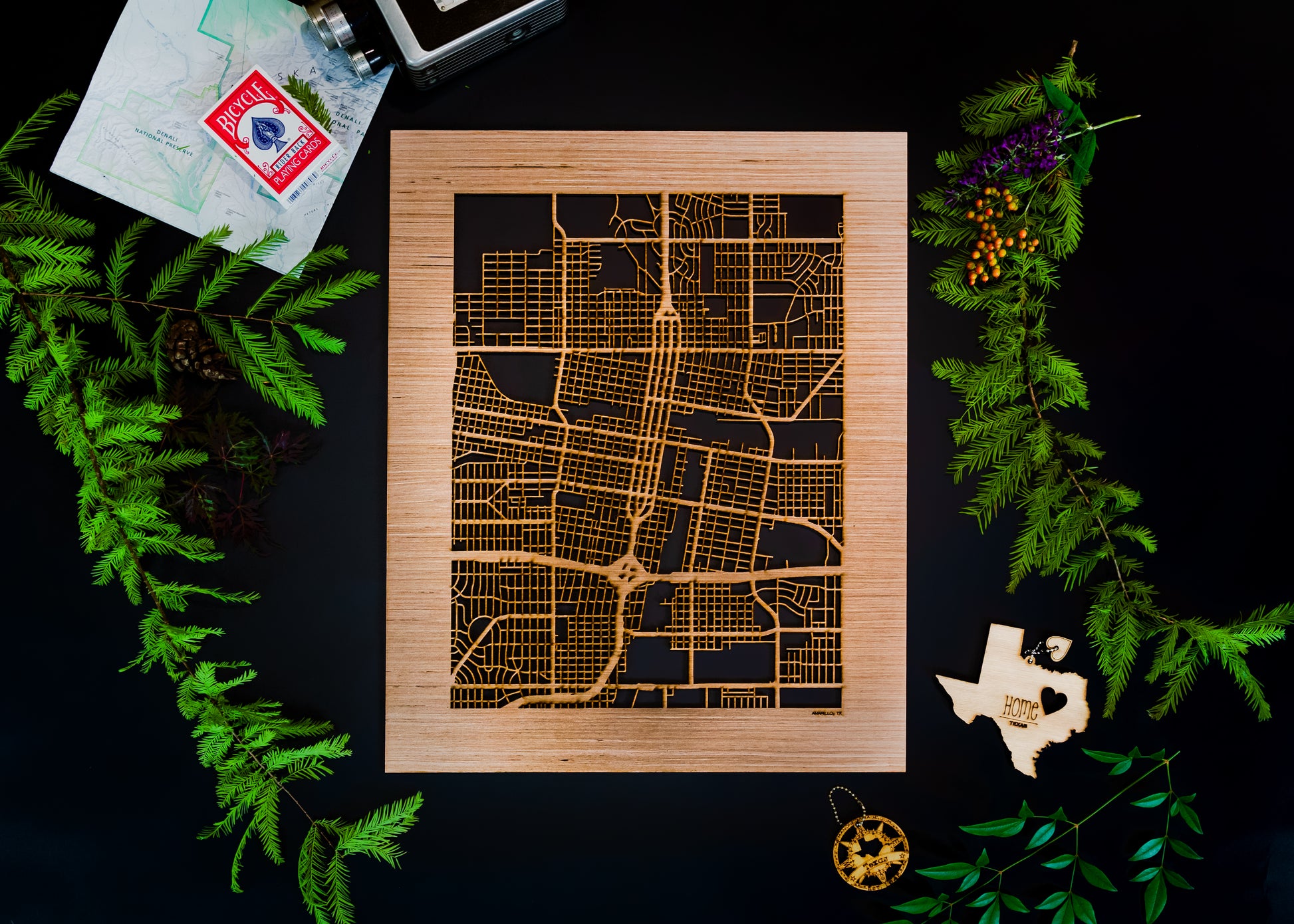 Wooden map art piece on a dark surface with greenery