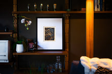Load image into Gallery viewer, Framed artwork on a shelf with decorative items in a dimly lit room