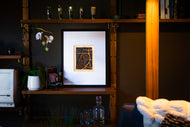 Framed artwork on a shelf with decorative items in a dimly lit room