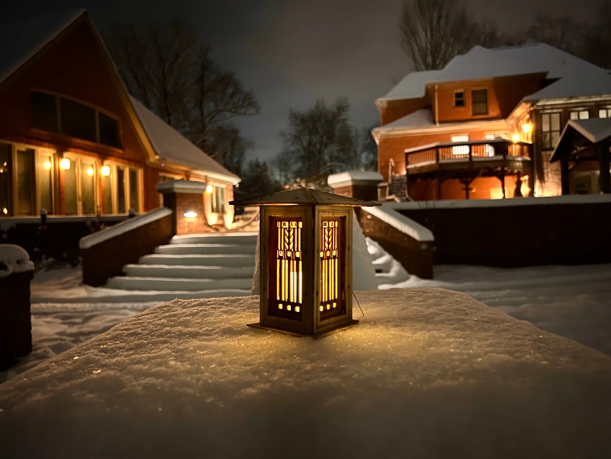 Decorative lantern on a snowy ground with a house in the background at night.