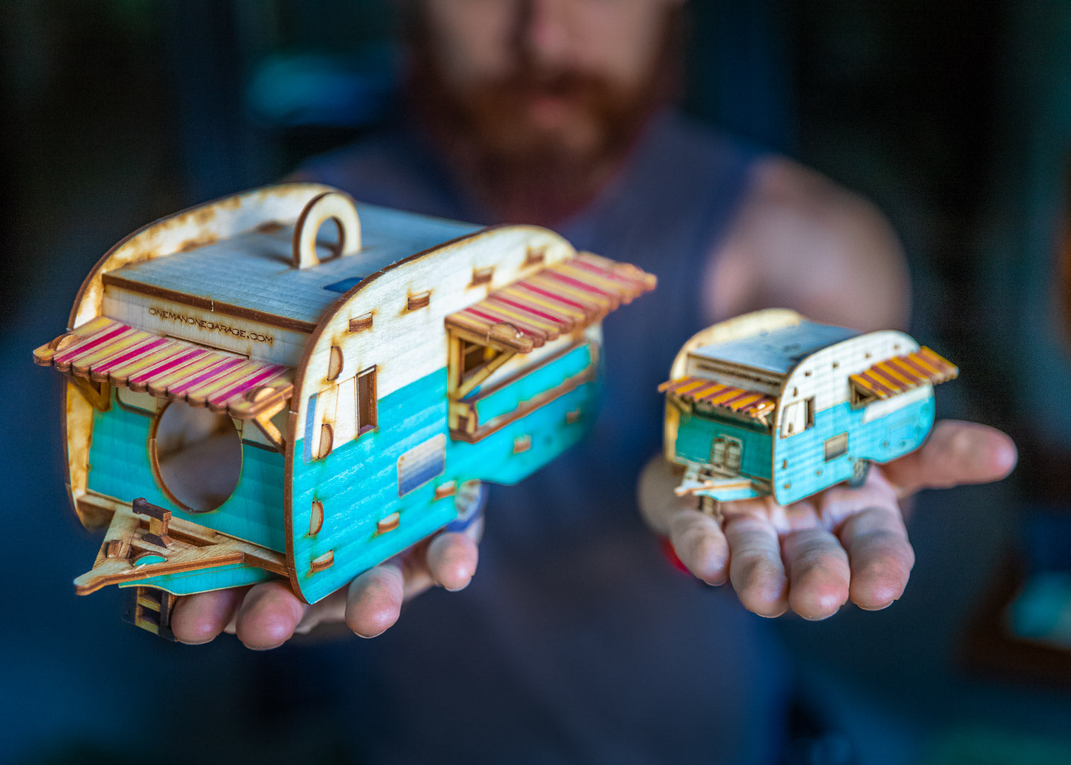 Hand holding a camper model on the left and a miniature version on the right, designed as desktop decor, showing scale and color options
