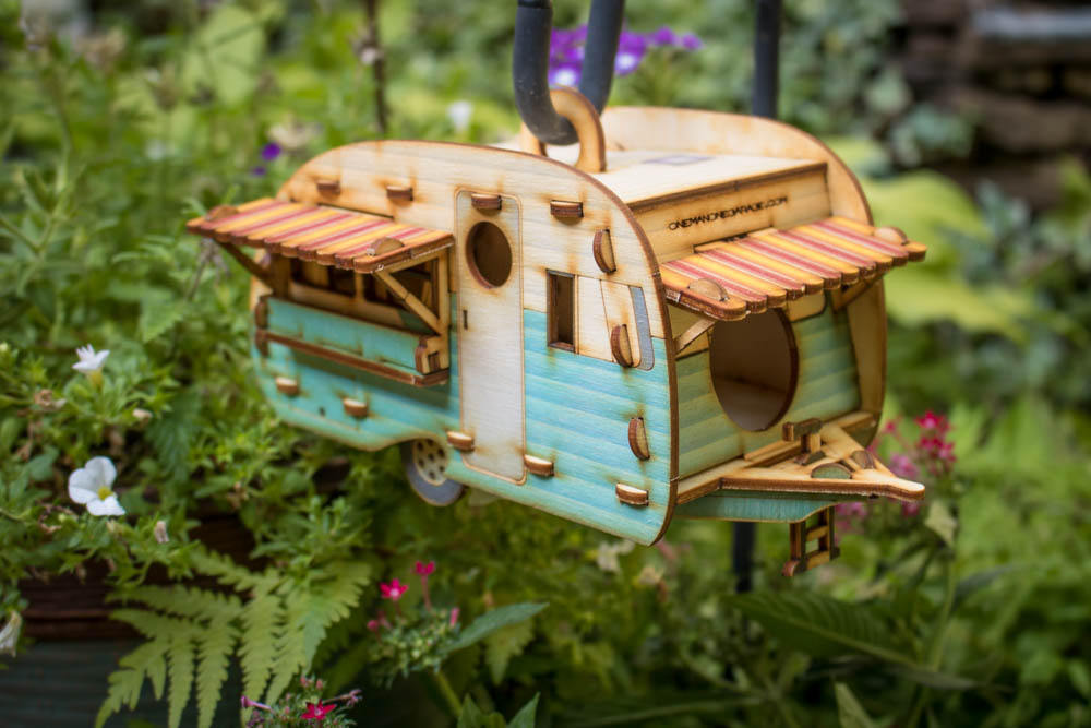 painted wooden camper birdhouse hanging among green foliage in garden setting
