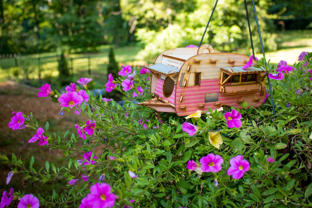 painted camper birdhouse hanging above colorful flowers in garden environment