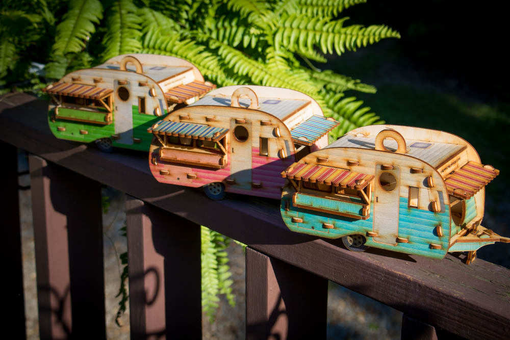 set of camper birdhouses in different colors displayed side by side on outdoor railing, details show their different colors; green, pink, and teal. 