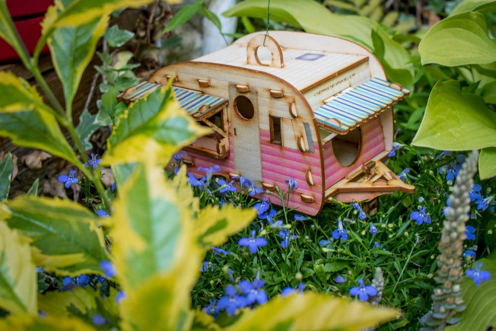 wooden camper birdhouse in pink pastel finish hanging among flowers and garden plants