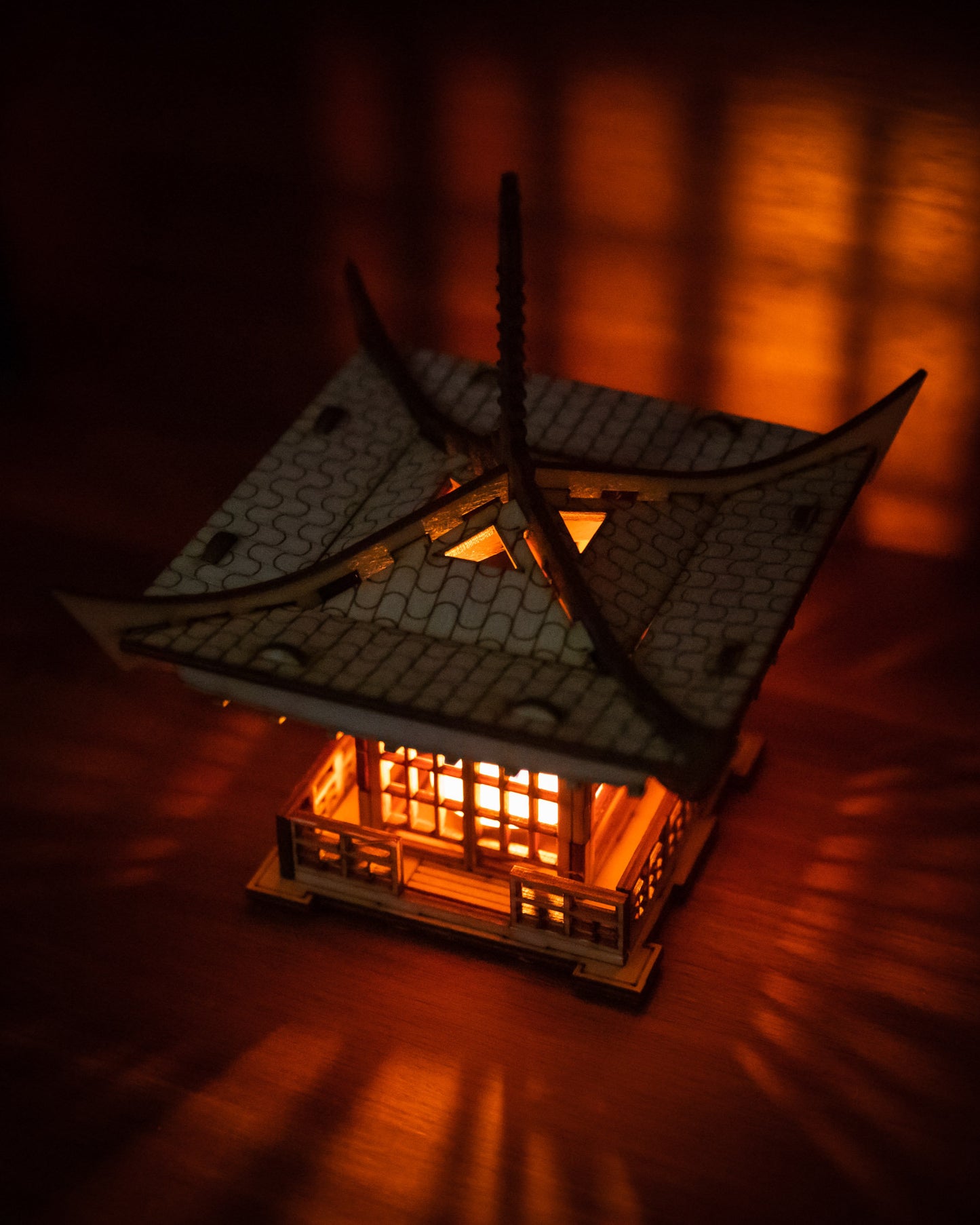 Pagoda-style candle holder glowing in dark room casting dramatic patterned shadows from an LED tea light candle