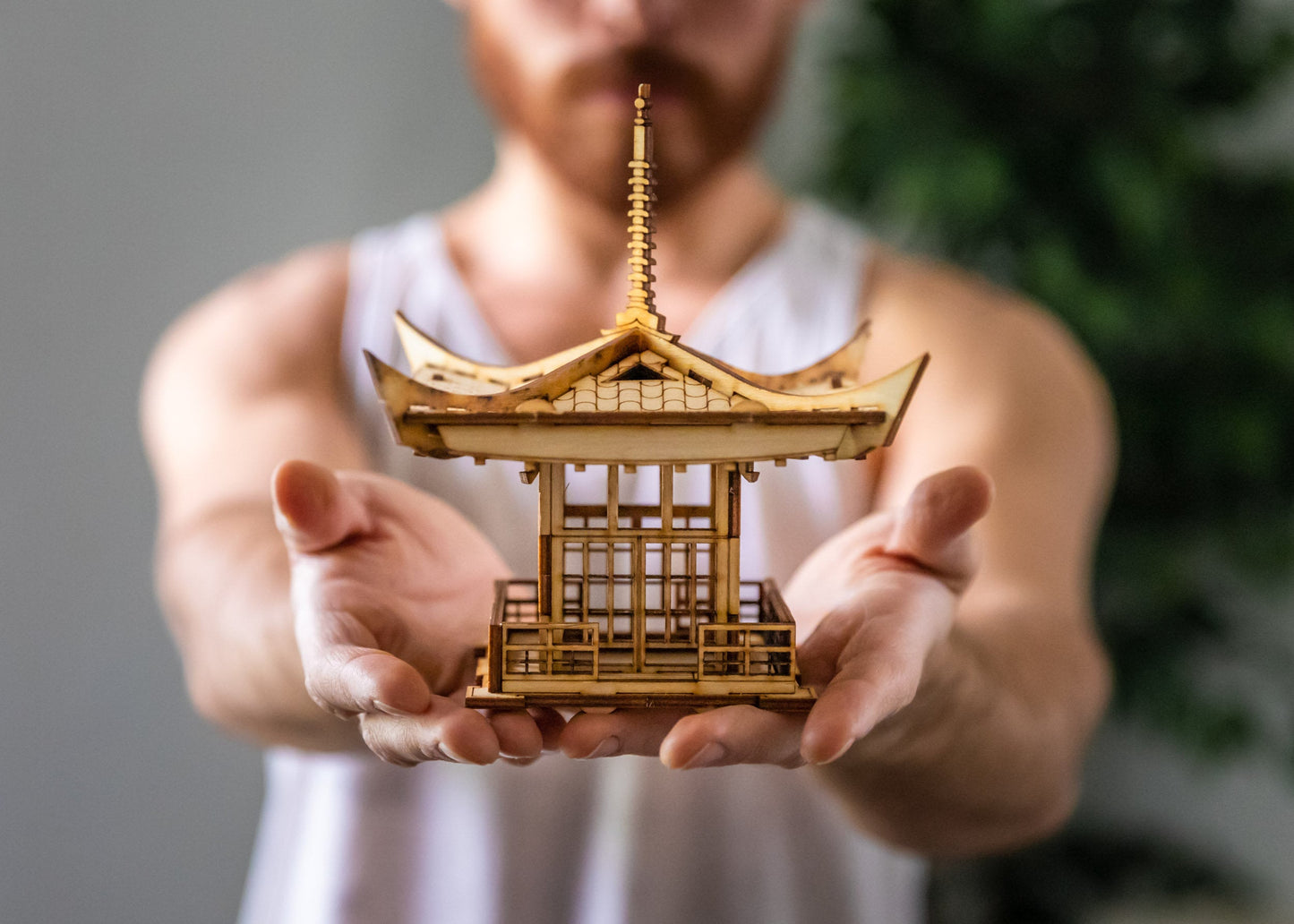 A person holding an assembled miniature Japanese pagoda lantern DIY wooden kit showing scale, with intricate details, primarily in a wooden color, indicating it is crafted from wood.