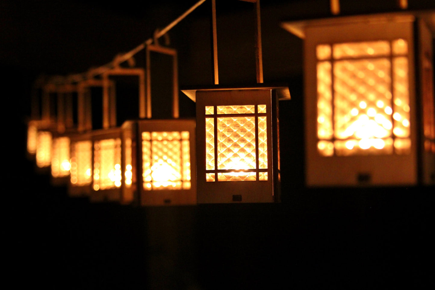 row of Craftsman-style lanterns illuminated with warm candlelight hanging in a dark setting